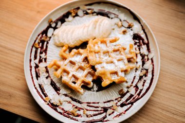 Sıcak bir kafe ortamında taze meyve ve serpiştirilmiş sosla servis edilen lezzetli Belçika waffleları.