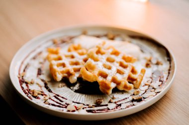 Belçika waffleları sabah saatlerinde rahat bir kafede dekoratif bir tabakta servis edilir.