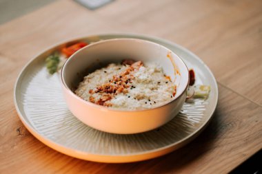 Üzerine kızarmış pastırma ve taze sebzelerle servis edilen parmesan soslu yulaf ezmesi.