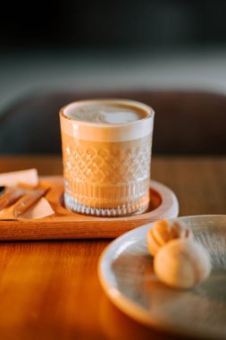 Sıcak latte, rahat bir kafe ortamında ahşap bir masada kurabiyelerle servis edilir.