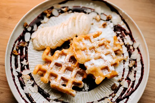 Lezzetli Belçika waffleları üzerine taze muz dilimleri ve çilek sosu serpiştirilmiş.