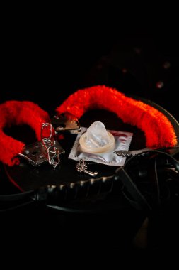 Karanlık bir yüzeyde hafif ışıklandırmalı renkli kelepçe ve prezervatif.