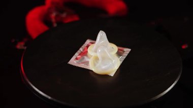 Yaratıcı görsel görüntü için kırmızı ışık efektleriyle siyah bir yüzey üzerinde dönen prezervatifler