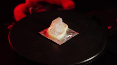 Yaratıcı görsel görüntü için kırmızı ışık efektleriyle siyah bir yüzey üzerinde dönen prezervatifler