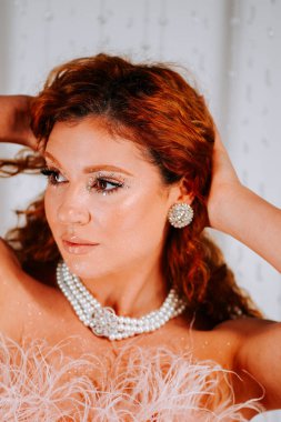 Beyaz arka planda, zarif giyinmiş kızıl saçlı bir kadının moda portresi.