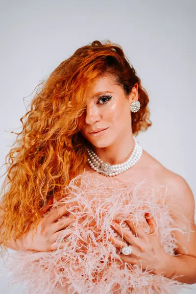 Canlı kızıl saçlı bir kadın beyaz bir arka plana karşı şık bir şekilde poz verir.