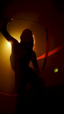 Kadın jimnastikçi neon ışıklarının altında kurdeleyle ritmik jimnastik yapıyor.