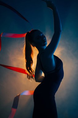 Kadın stüdyo seansı sırasında dinamik ışıklandırmada kurdelelerle ritmik jimnastik yapıyor.