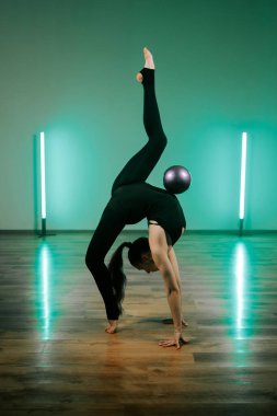 Kadınlar etkileyici yoga pozu ve top ile ritmik jimnastik becerileri sergiliyor.