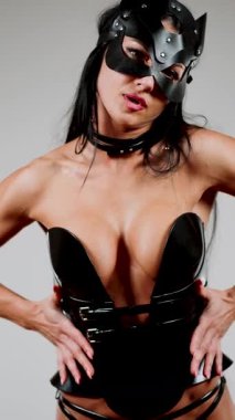 Modern stüdyo ortamında BDSM kedi maskesi ve deri korse performansı