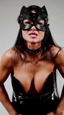 Deri korse ve kedi maskeli BDSM modeli stüdyo ortamında güvenle poz veriyor