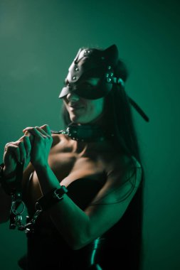 Kedi maskeli ve kelepçeli bir kadın bunaltıcı bir ortamda neon ışıkların altında poz veriyor.