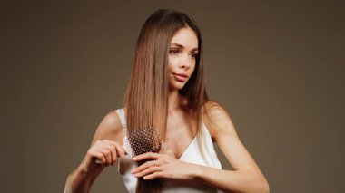 Sakin bir öğleden sonra, stüdyo ortamında uzun saçlarını tarayan bir kadın.
