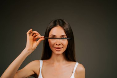 Tarafsız bir geçmişe sahip bir stüdyoda poz verirken makyaj fırçası gösteren bir kadın.