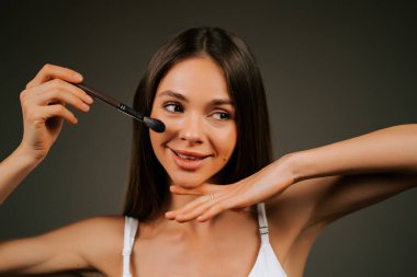 Kadın, akşam vakti stüdyo ortamında fırçayla makyaj yapıyor.