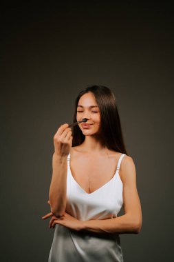 Kadın, makyaj fırçasıyla güzellik gösterisi için minimalist bir ortamda güven içinde poz veriyor.