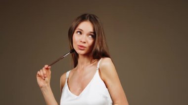 Stüdyo ortamında makyaj fırçasıyla poz veren bir kadın.