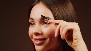 Yumuşak ışıklı bir odada kaşlarını fırçalayan bir kadın.