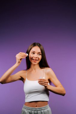 Kadın canlı mor arka planda pipetle yüz serumu uyguluyor.