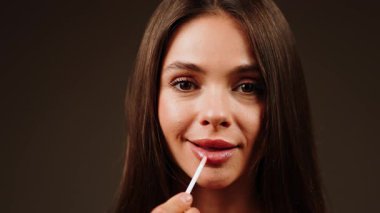 Kadın, iç mekânda yeni bir makyaj için dudak parlatıcısı sürüyor.