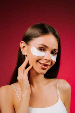 Göz bandı ve kolajen pedli kadın, stüdyoda parlak ışık altında parlayan bir cilt olduğunu gösteriyor.