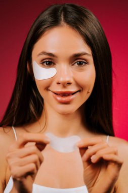 Göz altı kolajen pedlerini stüdyo ortamında parlak arkaplanı olan yeni cilt için kullanan güzel bir kadın.