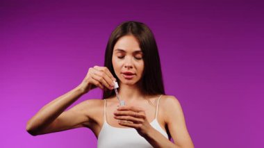 Parlayan cilt için mor arka planda yüz serumu uygulayan kadın.