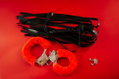 Yetişkin keşifleri ve oynamaları için canlı kırmızı bir arkaplanda BDSM oyuncakları görüntülendi