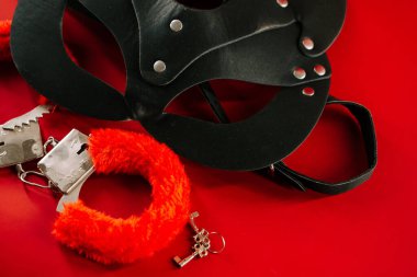 Koyu kırmızı arka planda sanatsal olarak dizilmiş BDSM oyuncakları ilgi çekici bir estetik deneyim yaratır