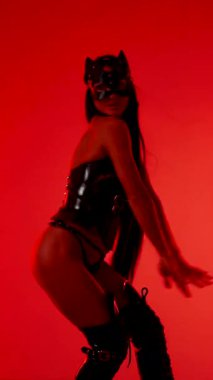 Kadın dansçı, kırmızı neon ışıkların altında kedi kostümü içinde etkileyici hareketler sergiliyor.