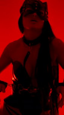 Kedi maskeli ve kelepçeli dansçı canlı kırmızı stüdyo ortamında gösteri yapıyor.