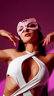 Kedi maskeli şık bir bayan dansçı pembe arka planda zarifçe poz veriyor.