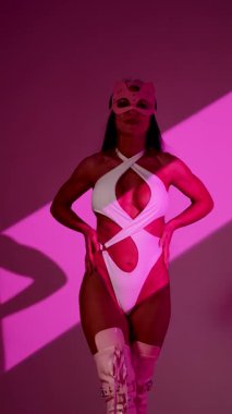 Beyaz elbiseli büyüleyici bayan dansçı ve pembe arka planda kedi maskesi etkileyici pozlar.