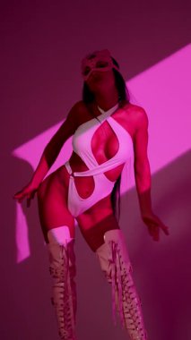 Beyaz elbiseli kadın dansçı ve kedi maskeli pembe arka planda gösteri yapıyor.