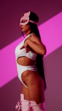 Kedi maskeli beyaz dansçı canlı bir şekilde pembe arka planda poz veriyor.