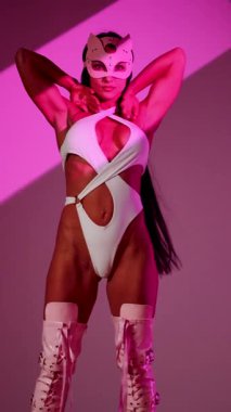 Beyaz elbiseli dansçı ve kedi maskeli dansçı dinamik pozlarla pembe arka planda gösteri yapıyor.