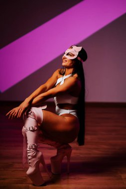 Pembe kedi maskeli kadın dansçı stüdyoda zarif bir şekilde poz veriyor.