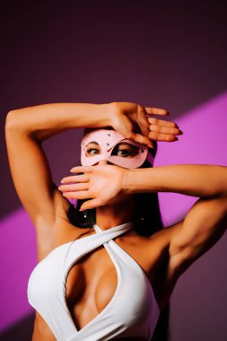 Pembe kedi maskesi takan kadın dansçı dramatik ışıklandırmayla bir stüdyoda gösteri yapıyor.