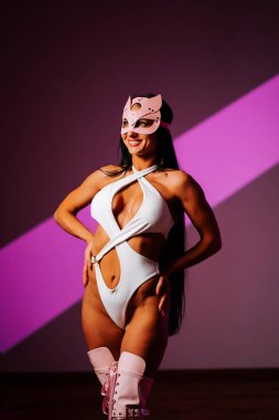 Kadın dansçı canlı pozlar sergiliyor. Şık kıyafetler içinde, pembe kedi maskesi takıyor.