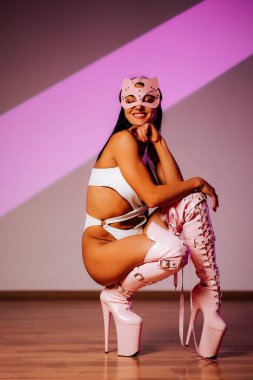 Pembe kedi maskeli dansçı ve açık kıyafet stüdyo ortamında güven içinde poz veriyor.