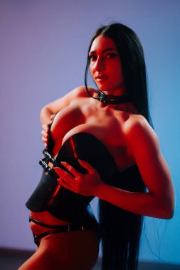 Kıvrımlı model modern bir stüdyo ortamında çarpıcı ışıklandırmayla şık bir kıyafet içinde poz veriyor.