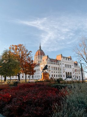 Macar Parlamentosu Binası, güneşli bir günde sonbahar ağaçları ve canlı bahçelerle çevrelenmiş.