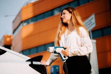 Kadın güpegündüz şarj istasyonunda elektrikli arabayı şarj ediyor.