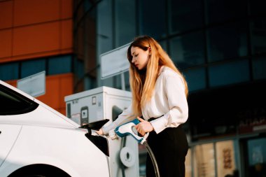 Gündüz vakti şehir merkezinde kadın elektrikli araba şarj ediyor.