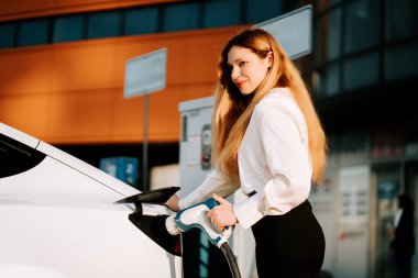 Gündüz vakti modern bir mekanda bir kadın elektrikli arabayı şarj ediyor.