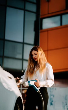 Gündüz vakti bir şarj istasyonunda kadın elektrikli araba şarj ediyor.