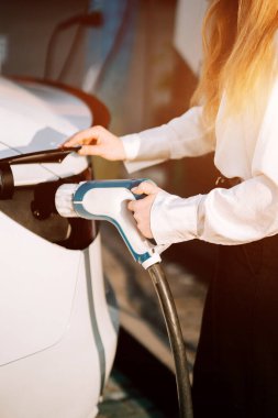 Dışarıda gündüz vakti şarj istasyonunda elektrikli bir aracı şarj eden bir kadın.