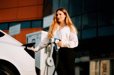 Kadın, akşam saatlerinde şarj istasyonunda elektrikli araç şarj ediyor.