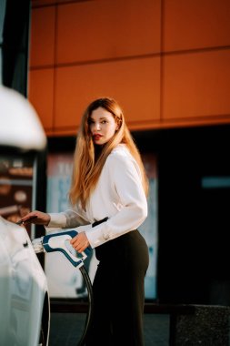 Öğleden sonra bir kadın elektrik istasyonunda elektrikli araba şarj ediyor.