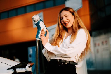 Kızıl saçlı genç bir kadın alışveriş merkezinin yakınındaki bir istasyonda elektrikli arabasını şarj ediyor.